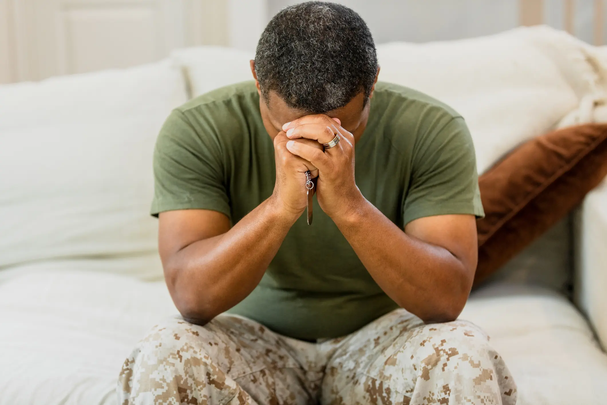 Male veteran sits alone in the living room holding his head in his hands.
