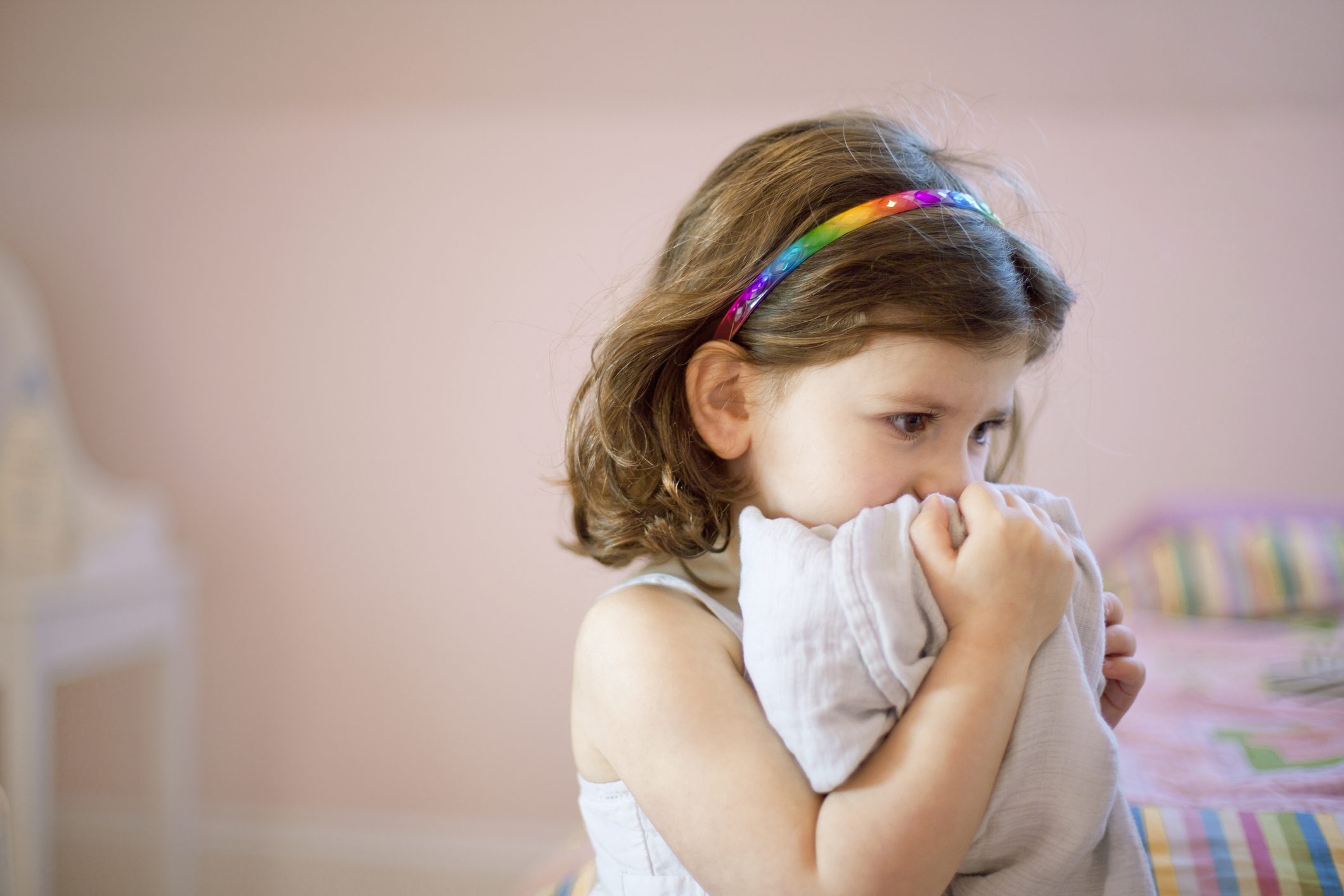 Unhappy little girl hugs pillow in her room.